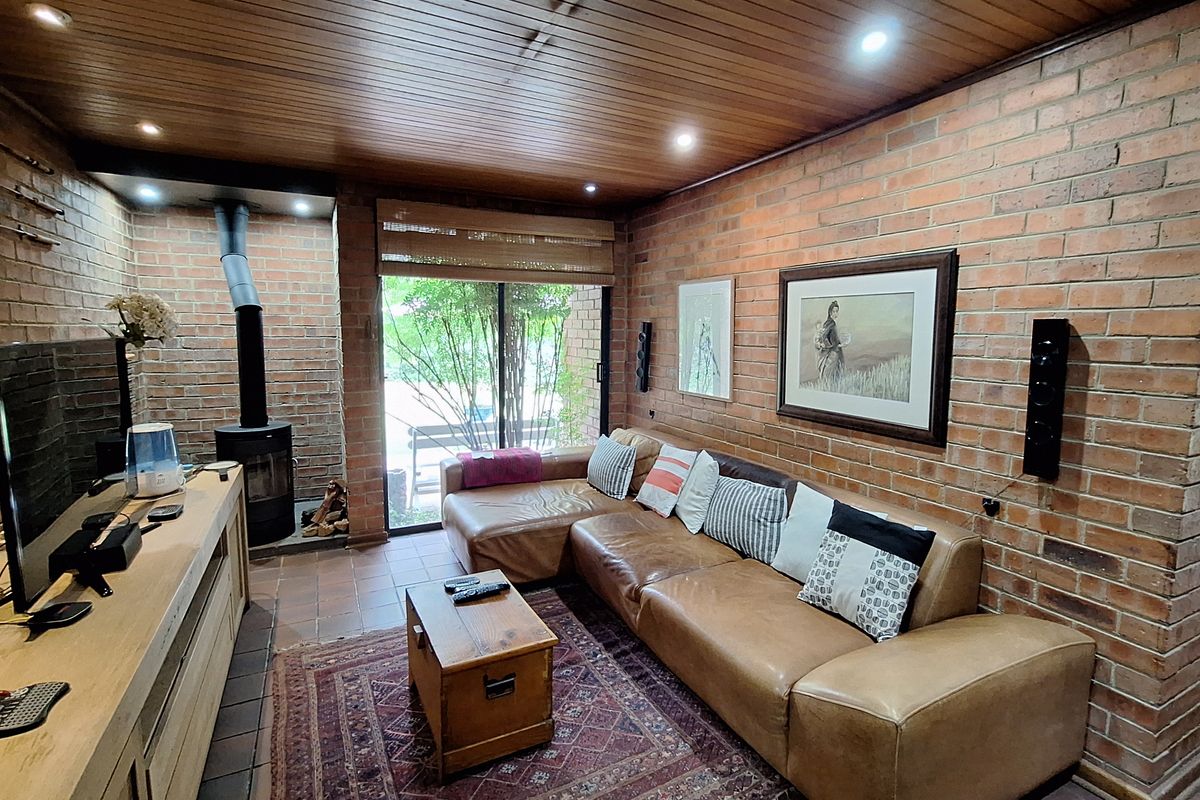 Cozy living room featuring exposed brick walls, a wood-burning fireplace, timber-paneled ceiling with recessed lighting, and sliding glass doors leading to the outdoors.