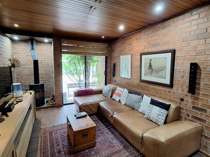 Cozy living room featuring exposed brick walls, a wood-burning fireplace, timber-paneled ceiling with recessed lighting, and sliding glass doors leading to the outdoors.