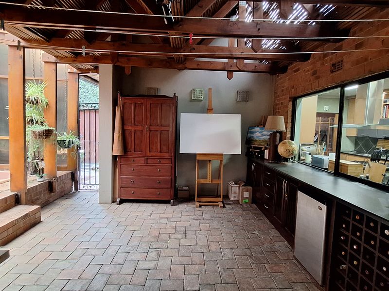 A covered patio area featuring exposed timber beams, brick flooring, and a built-in bar counter with integrated wine storage, overlooking the kitchen.