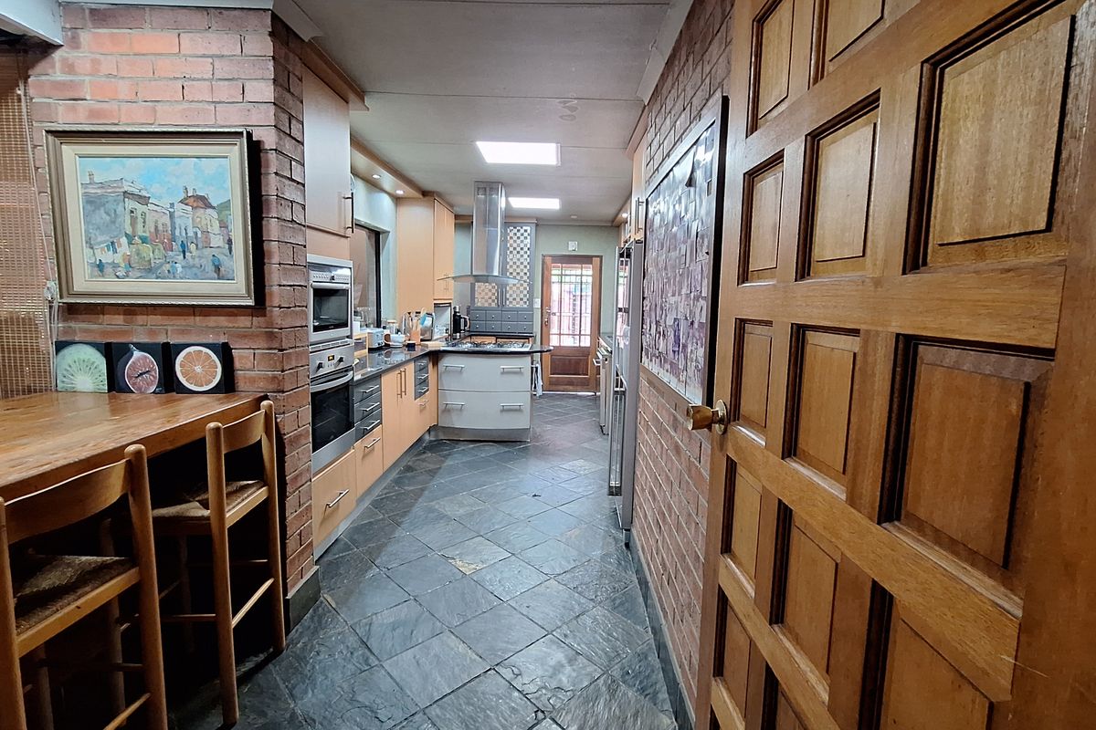 A galley-style kitchen featuring exposed brick walls, slate flooring, built-in cabinetry, integrated oven, and a stainless steel extractor fan.