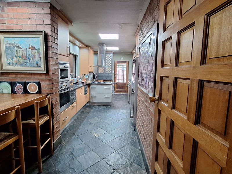 A galley-style kitchen featuring exposed brick walls, slate flooring, built-in cabinetry, integrated oven, and a stainless steel extractor fan.