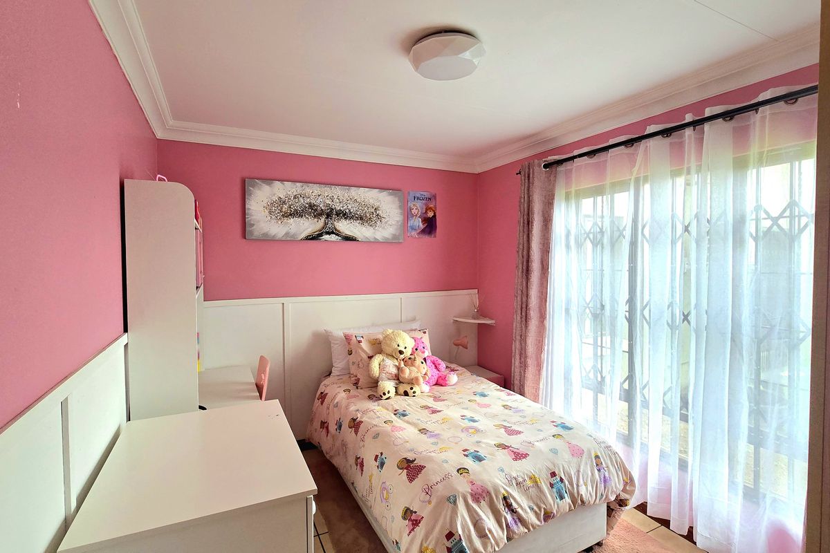 A bright bedroom featuring pink walls, white wainscoting, crown molding, and a sliding glass door with an integrated security gate.