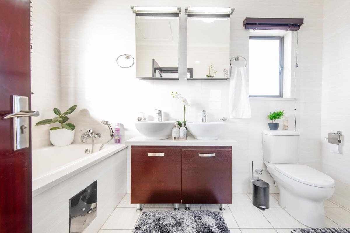 A well-maintained bathroom featuring a double vanity with vessel sinks, a built-in bathtub, and a modern toilet.