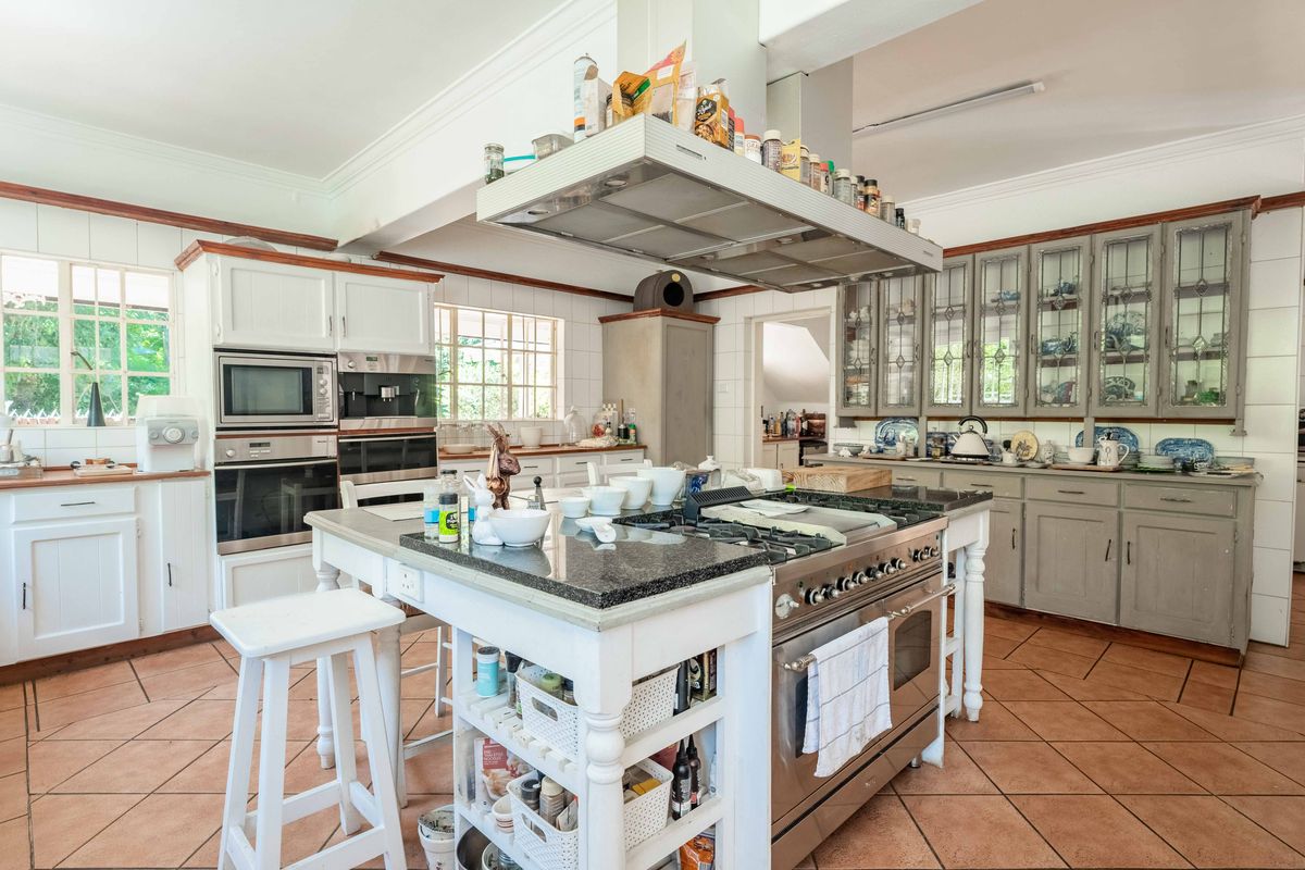 Spacious kitchen featuring a large central island with gas cooktop, built-in ovens, extensive cabinetry, and tiled flooring, offering a classic farmhouse aesthetic.