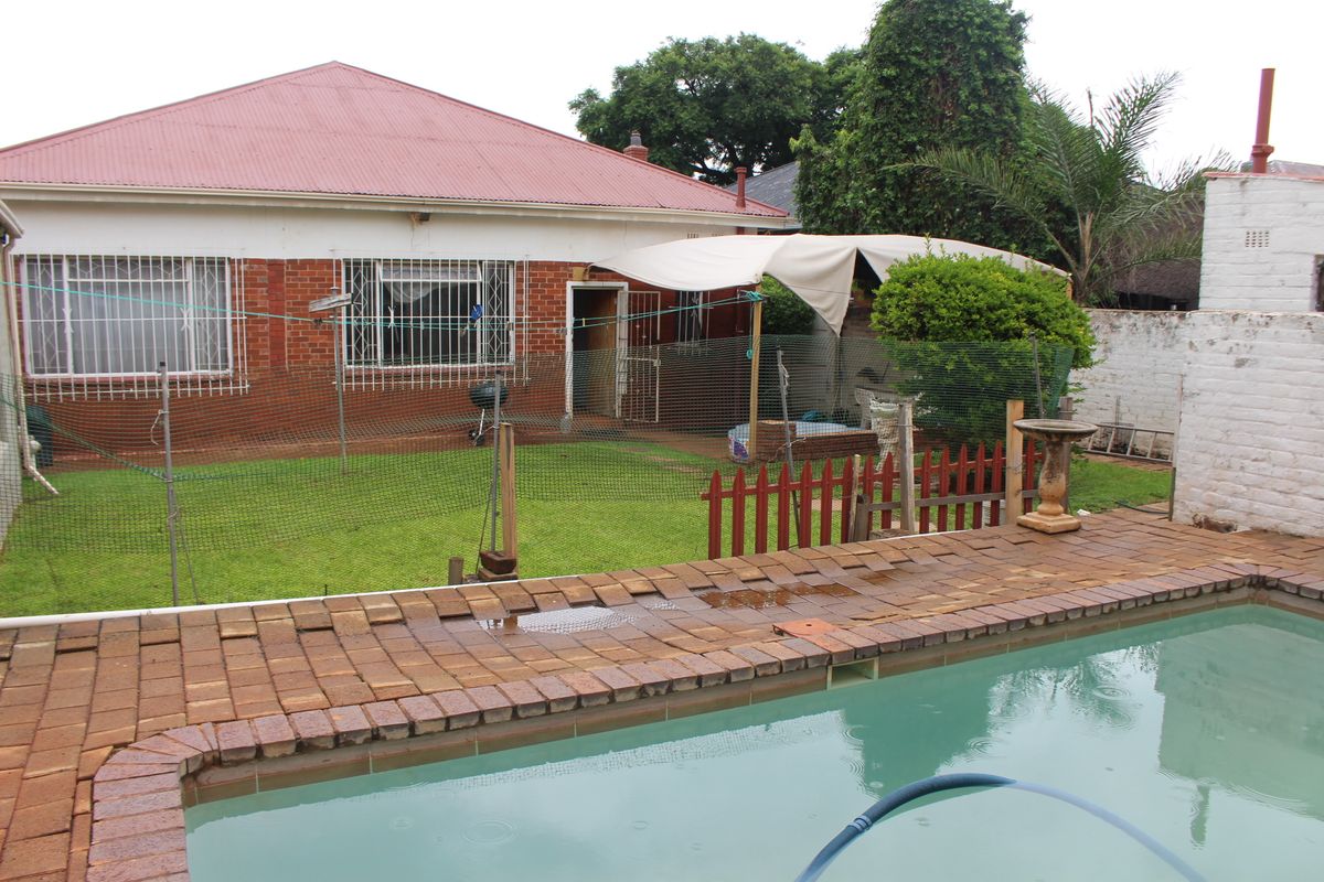 Rear view of the property featuring a swimming pool, brick paved surround, and a lawn area with a red metal roof house facade.