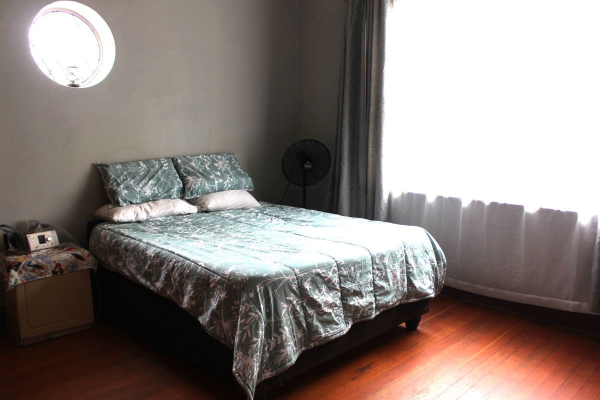 A bedroom featuring original hardwood flooring, a unique circular accent window, and a large window providing natural light.