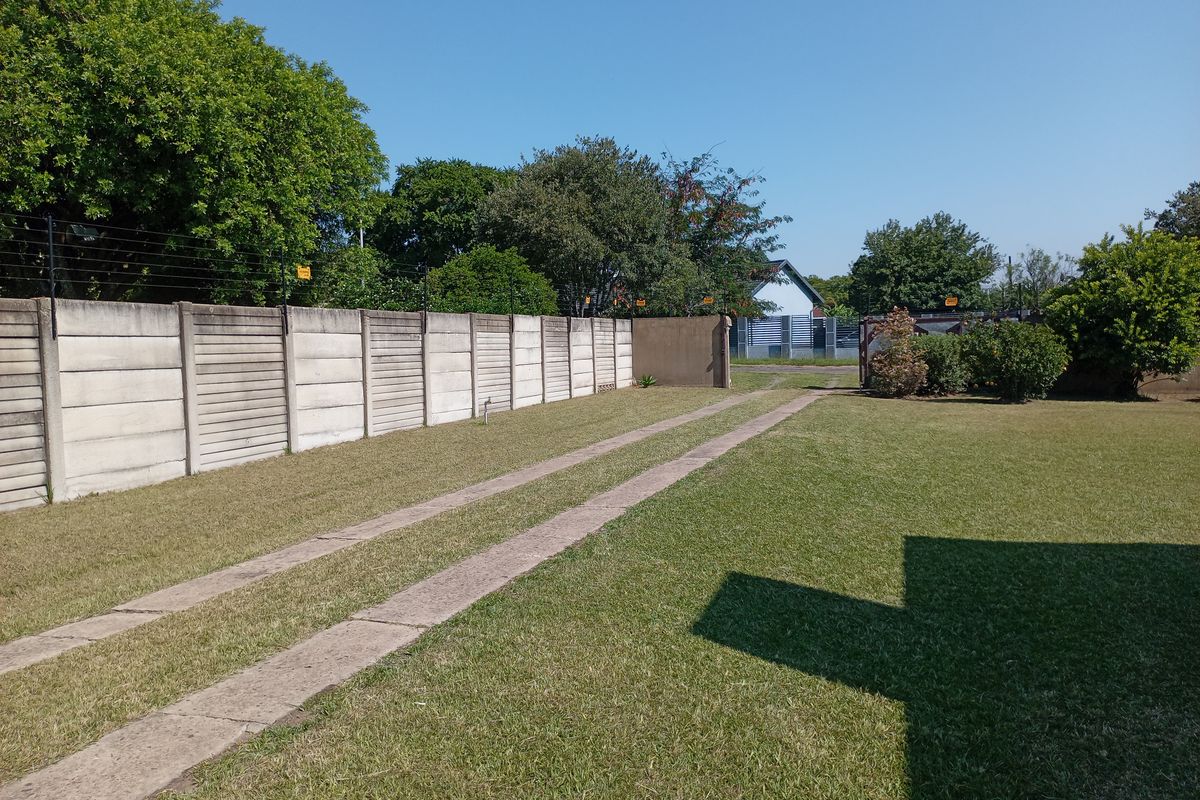 A spacious rear garden featuring a well-maintained lawn, concrete driveway tracks, and a secure precast concrete boundary wall with electric fencing.
