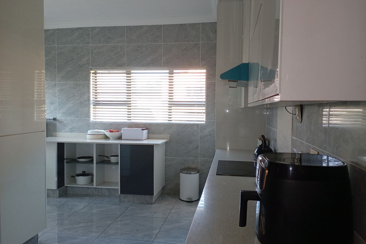 Modern kitchen featuring sleek white and dark cabinetry, stone countertops, tiled walls, and a functional layout with an integrated extractor fan.