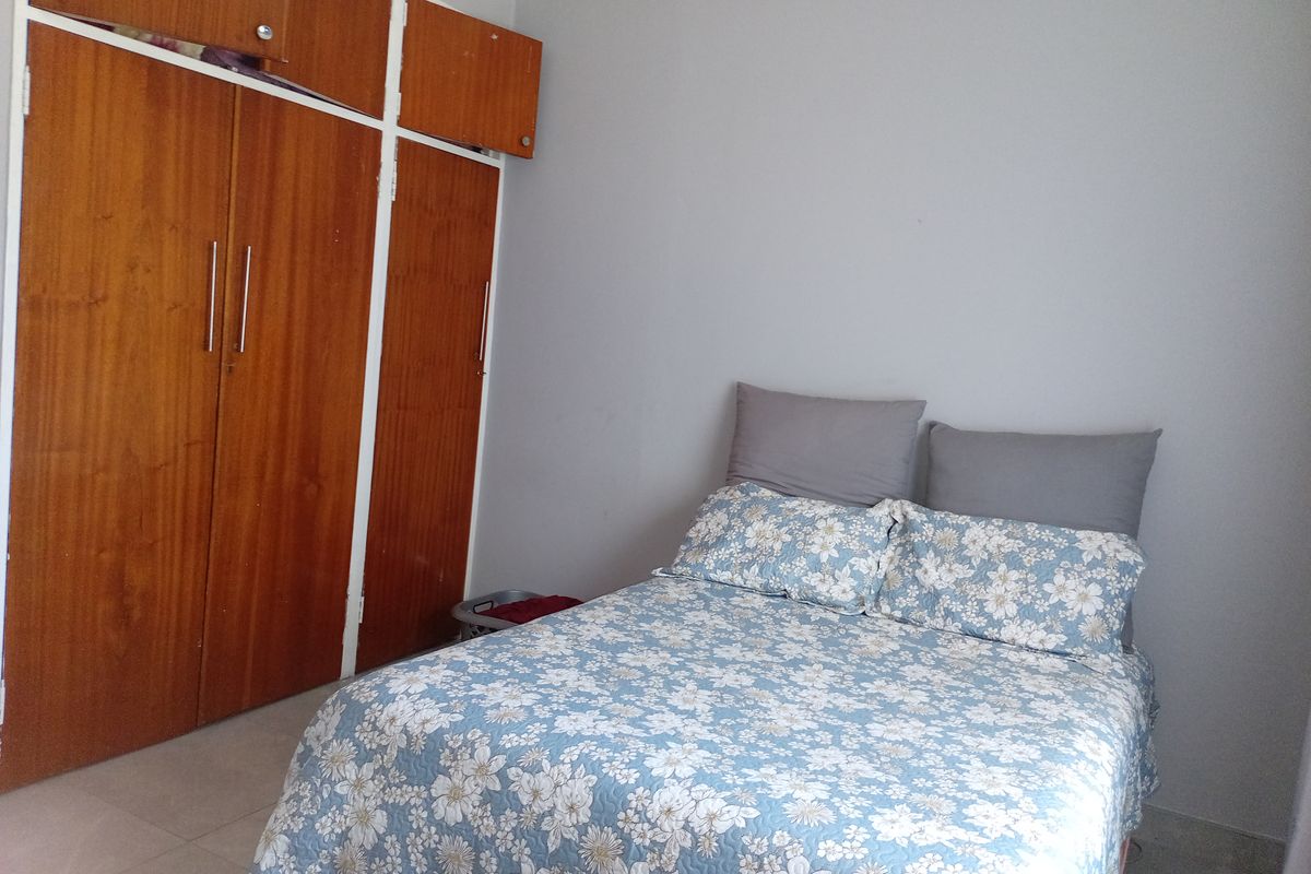 A bedroom featuring built-in wooden cupboards, tiled flooring, and neutral wall finishes.