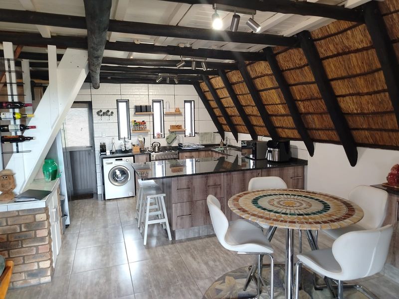 Open-plan kitchen and dining area featuring granite countertops, modern cabinetry, exposed timber beams, and a unique thatched ceiling design.