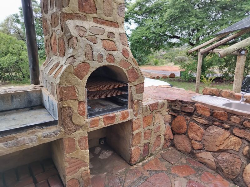 Outdoor patio area featuring a rustic stone-built braai, integrated fireplace, and a stainless steel sink set into stone masonry.