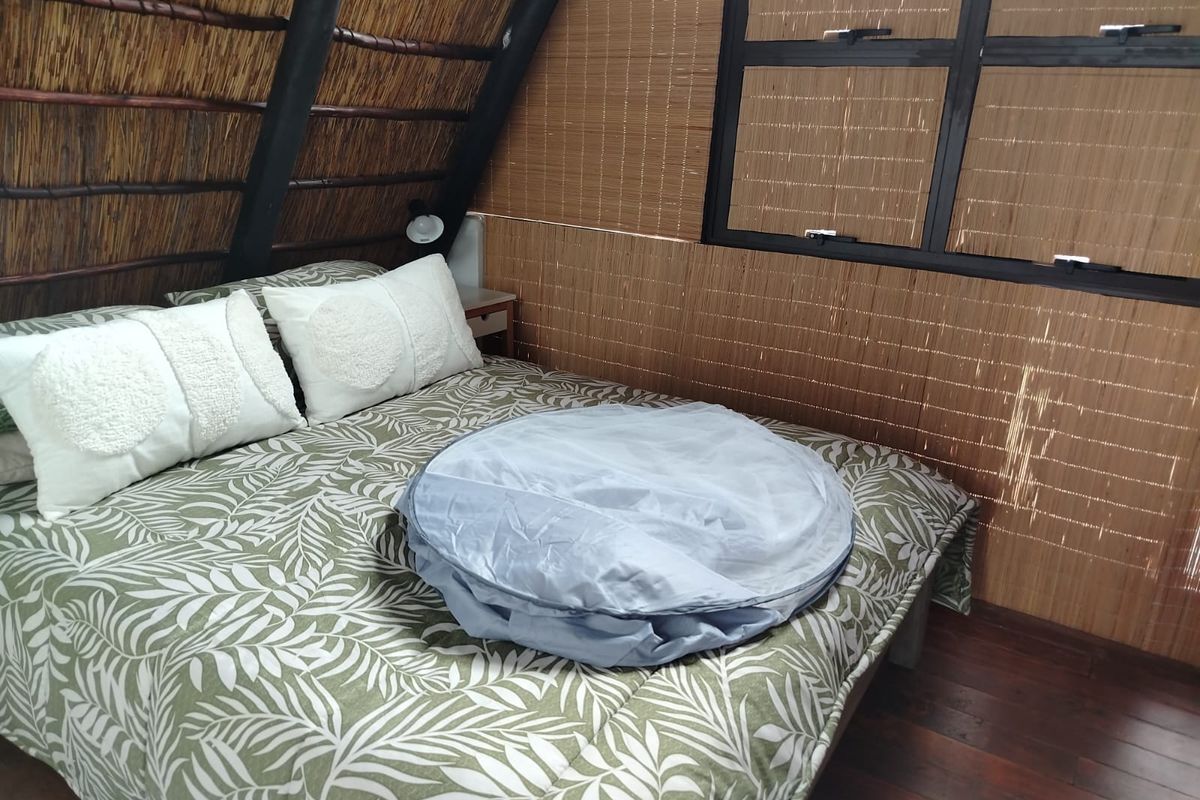 A bedroom featuring a unique A-frame design with a thatched roof, timber structural elements, and a casement window.