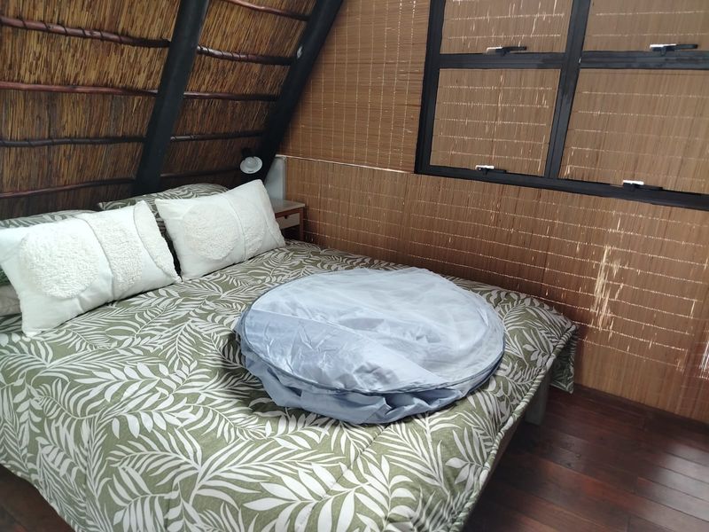 A bedroom featuring a unique A-frame design with a thatched roof, timber structural elements, and a casement window.