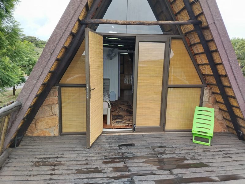 A rustic A-frame cabin balcony featuring timber decking, stone accents, and a thatched roof, providing access to the interior living space.