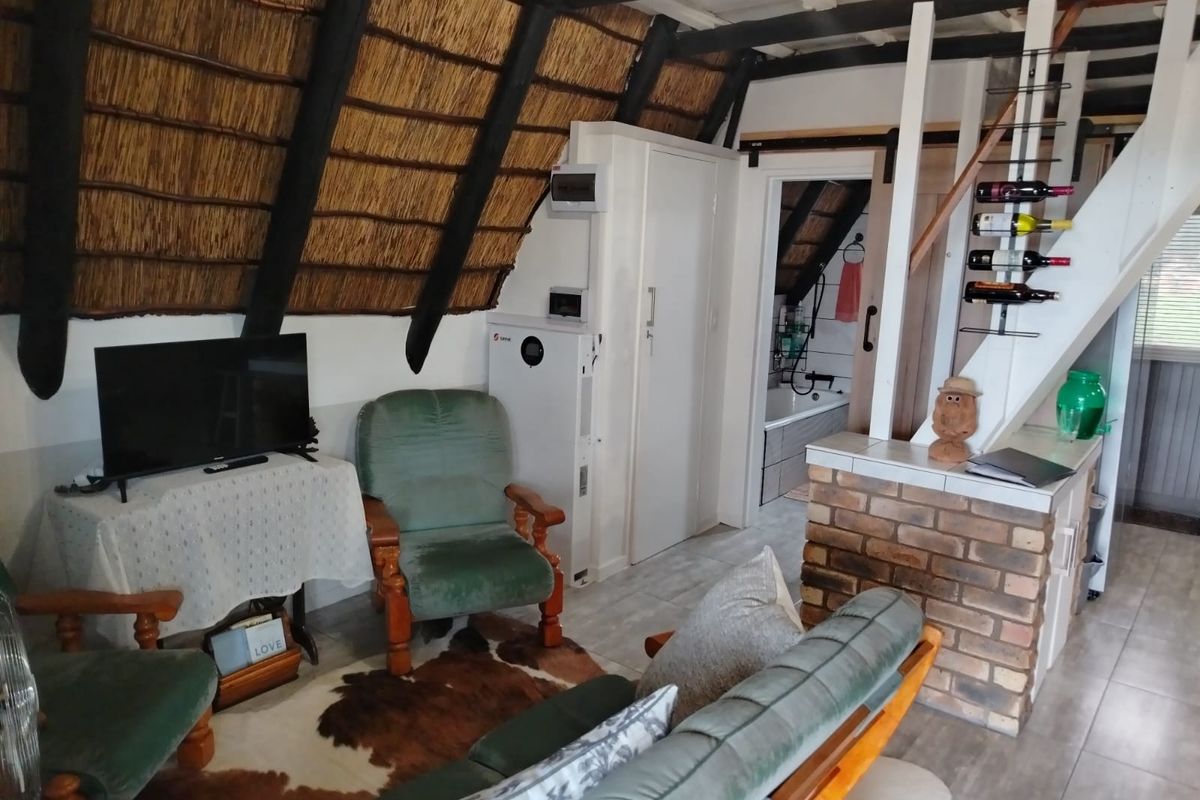 Living area featuring a rustic thatched roof with exposed timber beams, brick accents, and a staircase leading to an upper level.