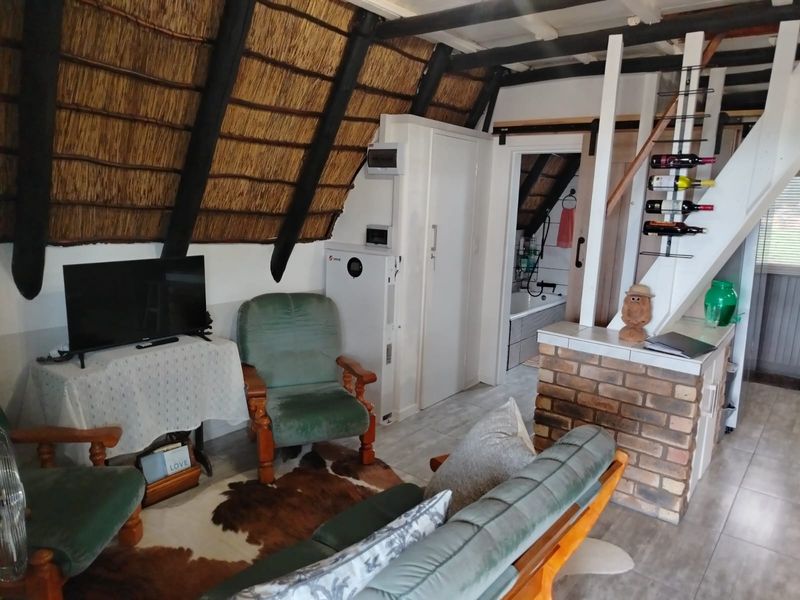 Living area featuring a rustic thatched roof with exposed timber beams, brick accents, and a staircase leading to an upper level.