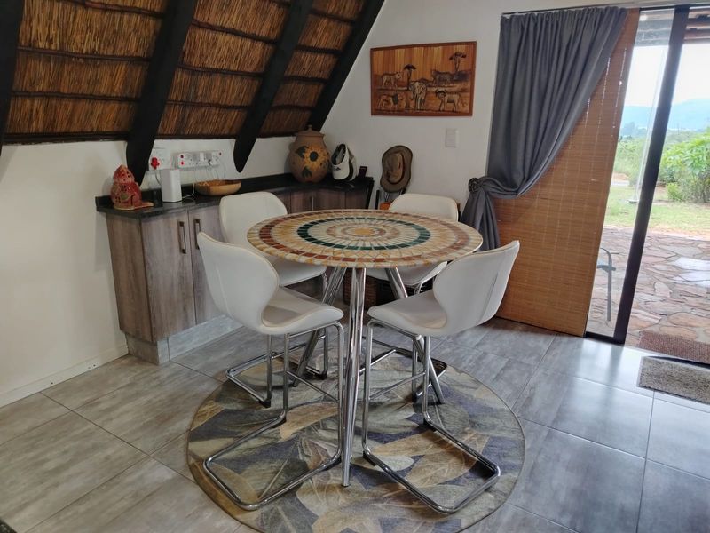 Dining area featuring a thatched roof, built-in cabinetry with stone countertops, tiled flooring, and direct access to an outdoor patio through a sliding door.