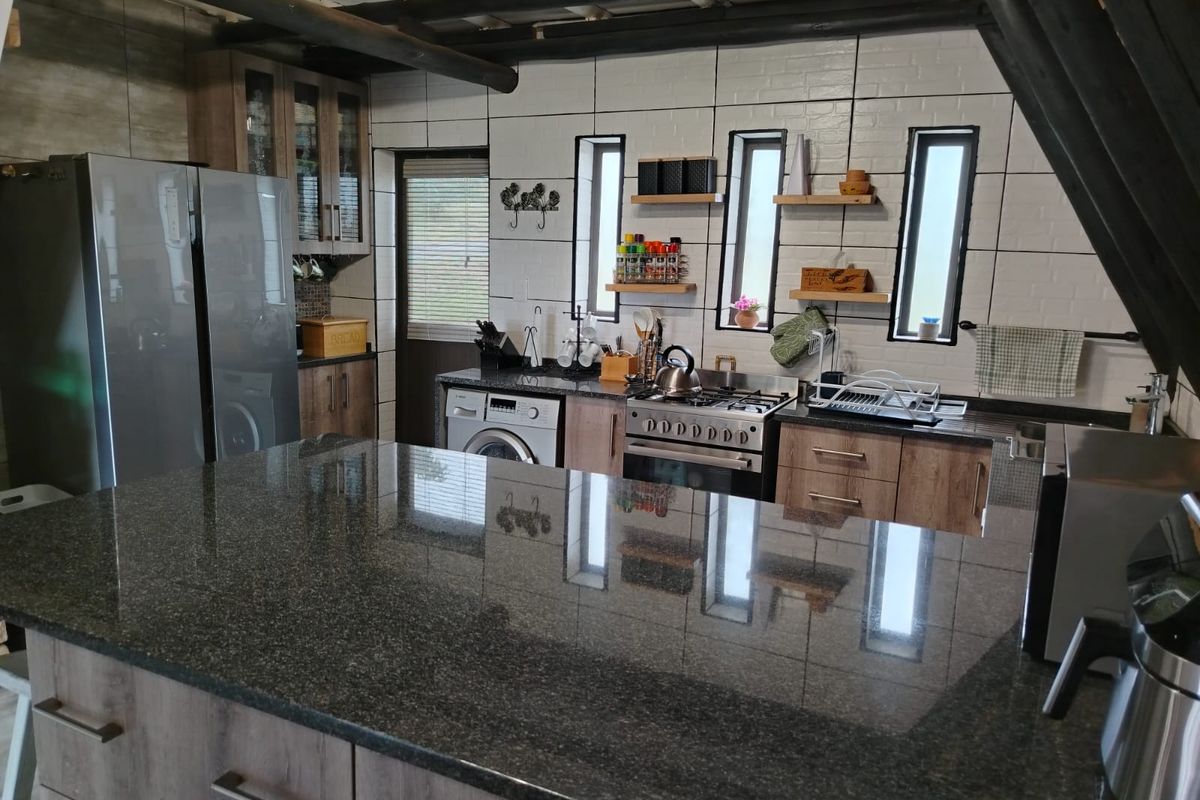 A well-appointed kitchen featuring a large granite island, modern cabinetry, gas stove, and exposed timber ceiling beams, offering a functional and stylish workspace.