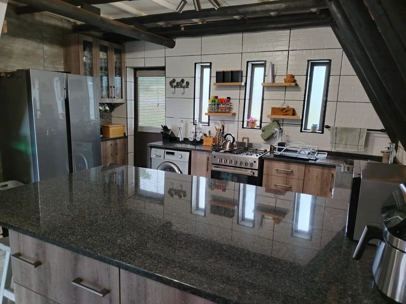 A well-appointed kitchen featuring a large granite island, modern cabinetry, gas stove, and exposed timber ceiling beams, offering a functional and stylish workspace.