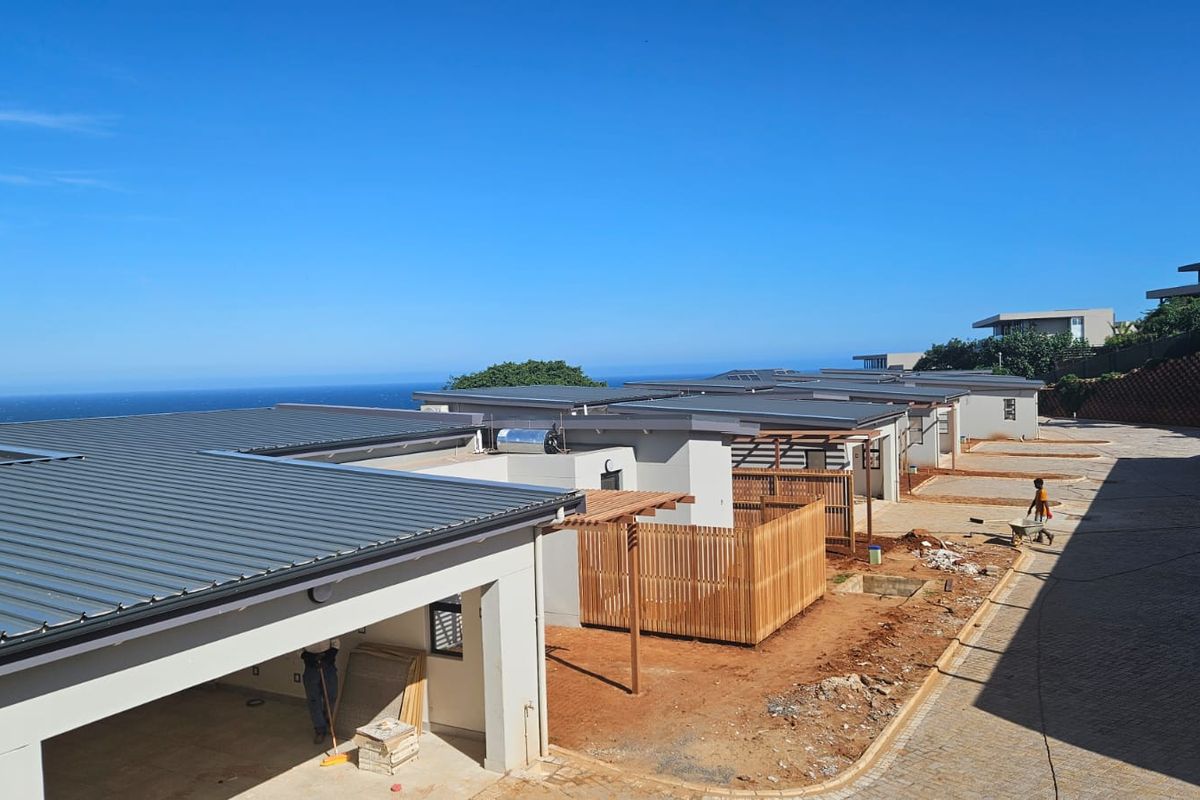 Exterior view of a modern apartment complex under construction, featuring metal roofing, timber pergolas, and ocean views.