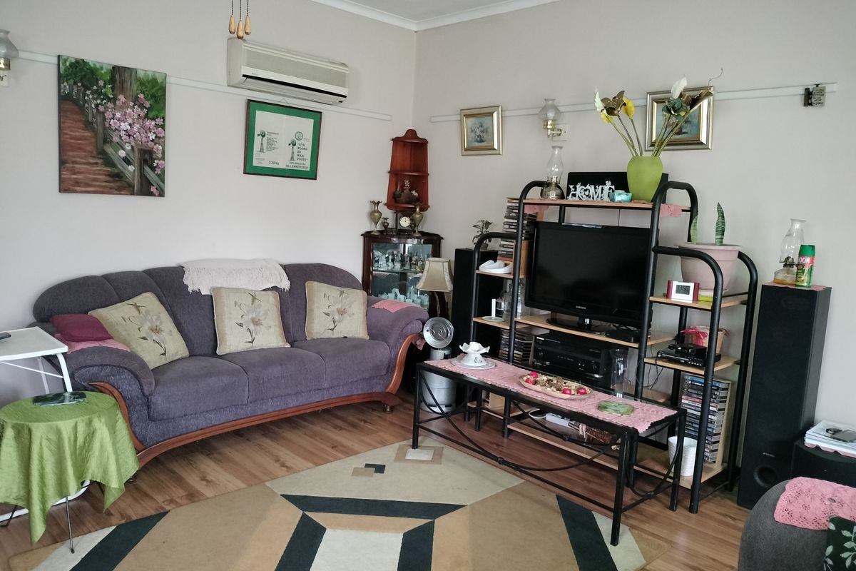 A comfortable living room featuring laminate flooring, a wall-mounted split-system air conditioner, and a traditional picture rail.