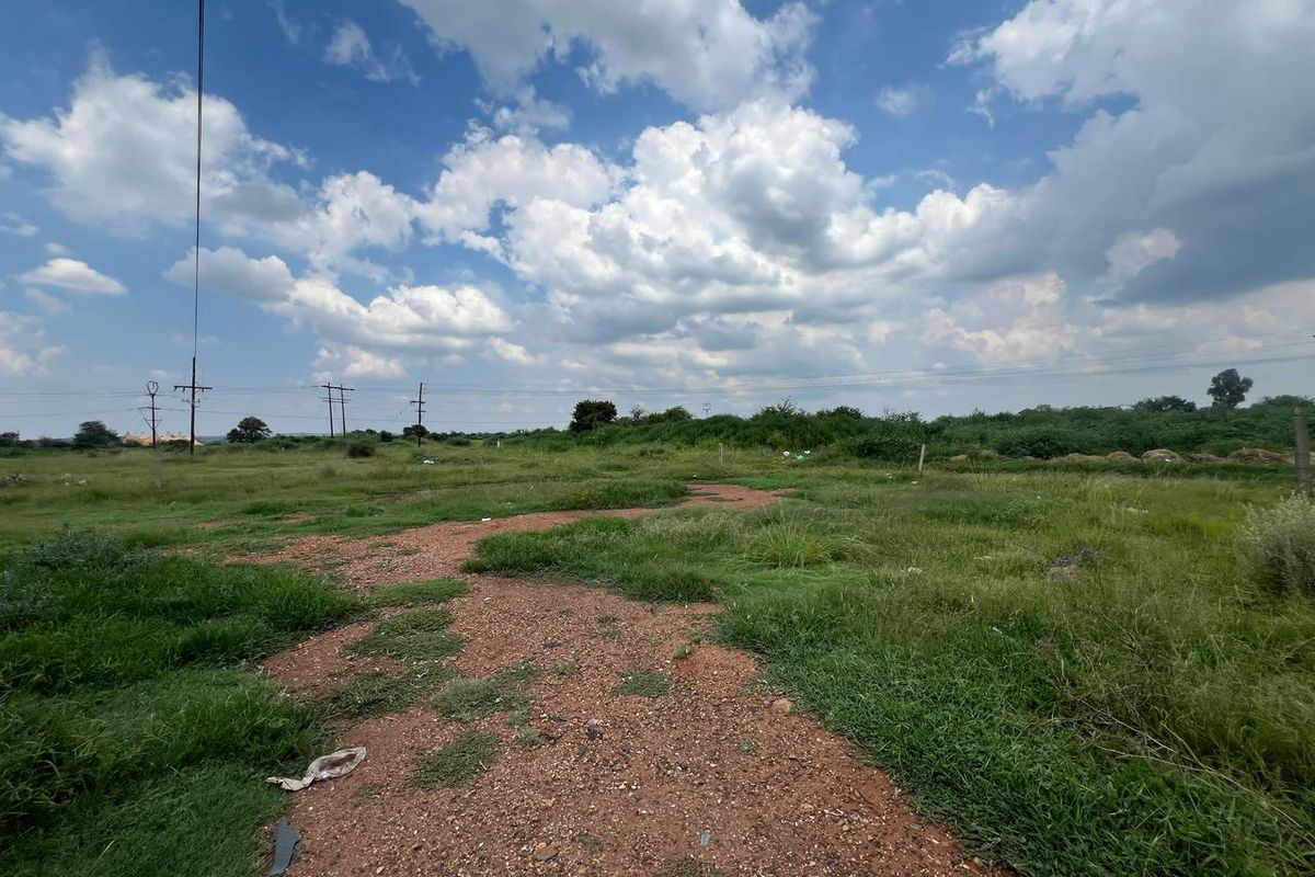 A vacant residential plot featuring natural grass cover and overhead power lines, offering a clear space for future development.