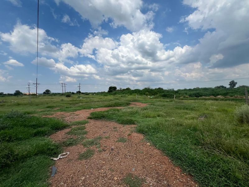 A vacant residential plot featuring natural grass cover and overhead power lines, offering a clear space for future development.