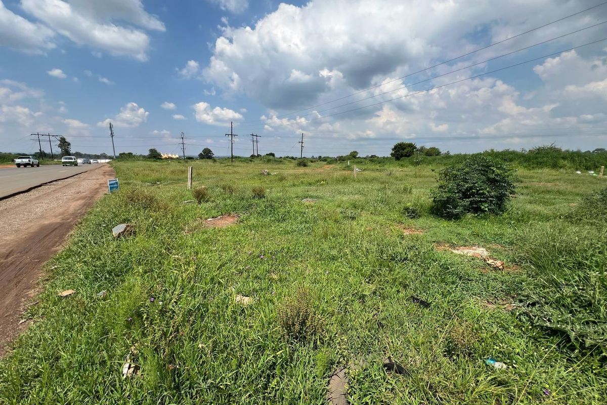 A vacant residential plot of land situated adjacent to a public road, featuring open grassy terrain and accessible utility infrastructure.