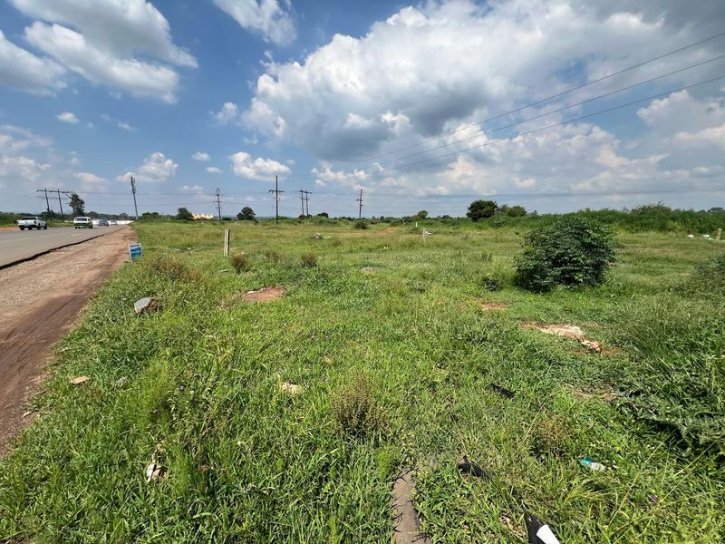 A vacant residential plot of land situated adjacent to a public road, featuring open grassy terrain and accessible utility infrastructure.