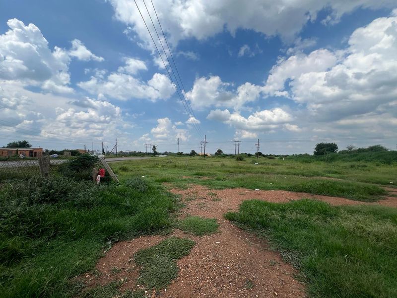 A vacant residential plot featuring natural grass cover, dirt access paths, and overhead utility lines, offering a clear view of the surrounding landscape.