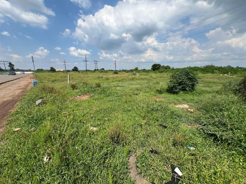 A vacant residential plot of land situated adjacent to a paved road, featuring open grassy terrain and overhead utility infrastructure.
