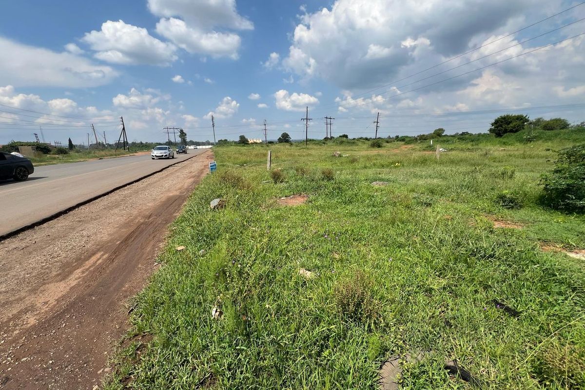 A view of the vacant residential land plot adjacent to the main road, featuring natural grass coverage and overhead utility lines.