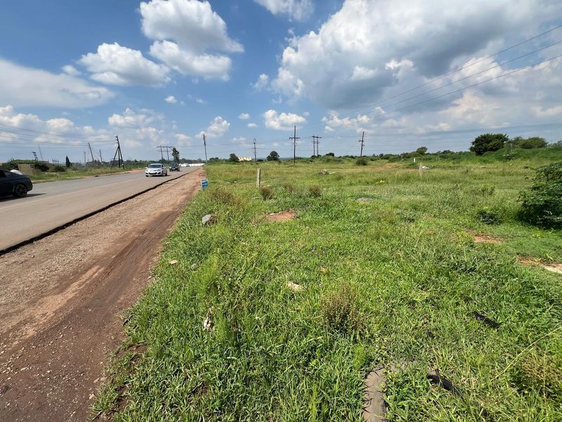 A view of the vacant residential land plot adjacent to the main road, featuring natural grass coverage and overhead utility lines.