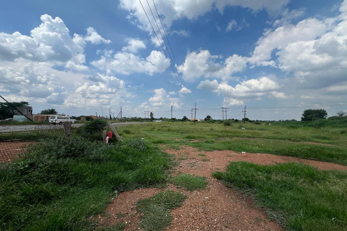 A view of a vacant residential plot featuring natural grass coverage, perimeter wire fencing, and overhead power lines.