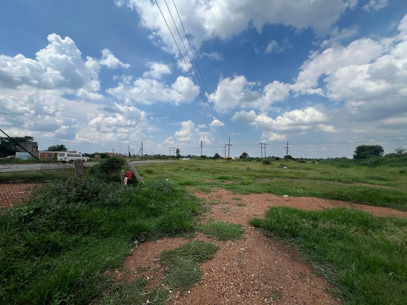 A view of a vacant residential plot featuring natural grass coverage, perimeter wire fencing, and overhead power lines.