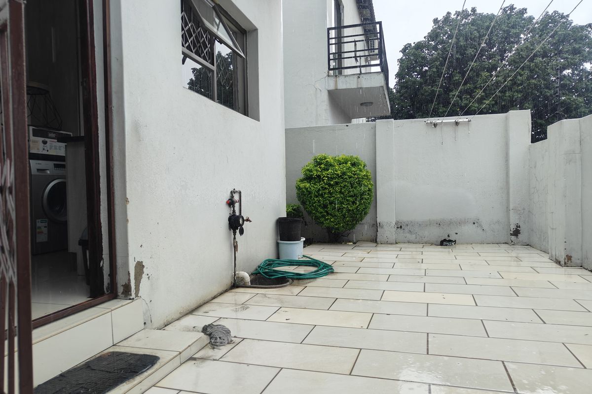 A paved rear patio area featuring a boundary wall, external water tap, and access to the interior laundry space.