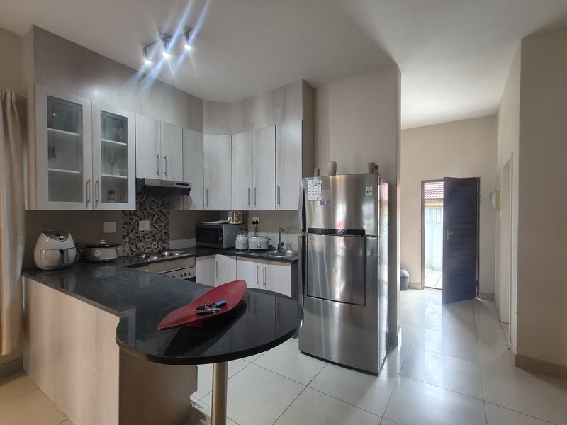 Modern kitchen featuring granite countertops, ample built-in cabinetry, integrated appliances, and tiled flooring, with direct access to an exterior doorway.