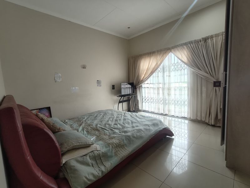 A bedroom featuring tiled flooring, a built-in cupboard, and a sliding glass door with a security gate leading to an outdoor area.
