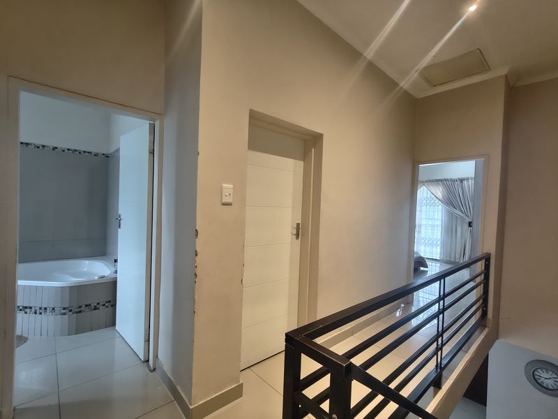 A bright upper-level hallway featuring tiled flooring, a modern metal balustrade, and access to adjacent rooms including a bathroom.