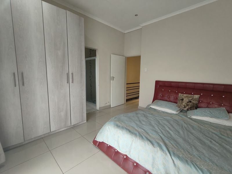 Spacious bedroom featuring large built-in wardrobes, neutral tiled flooring, and direct access to an en-suite bathroom.