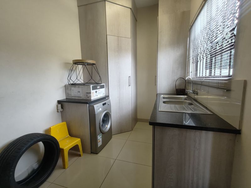 A functional laundry room featuring built-in cabinetry, a stainless steel sink with granite countertops, and tiled flooring.