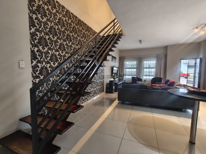 Spacious open-plan living area featuring a modern open-tread staircase with metal balustrade, tiled flooring, and large windows with security gates.