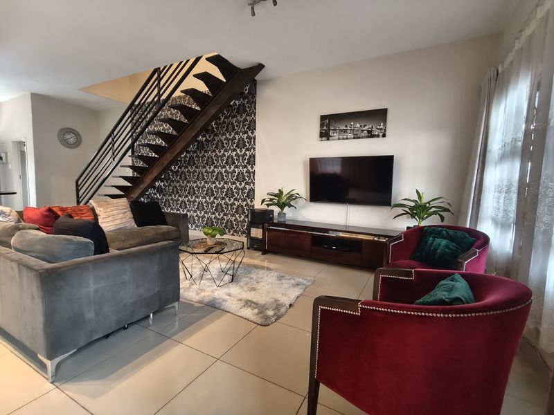 Spacious living room featuring an open-tread staircase with metal balustrade, tiled flooring, and a decorative feature wall.