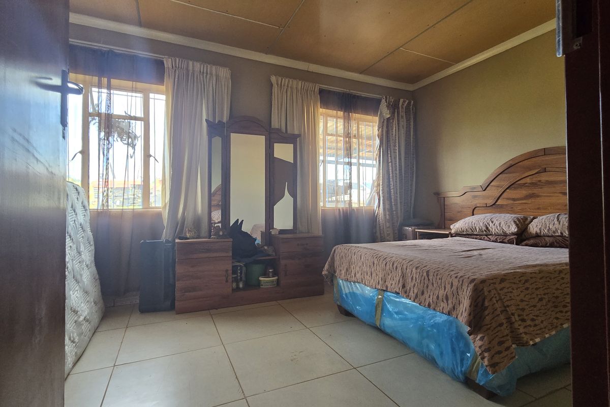 A bedroom featuring tiled flooring and a paneled ceiling, with natural light entering through two windows fitted with security bars.