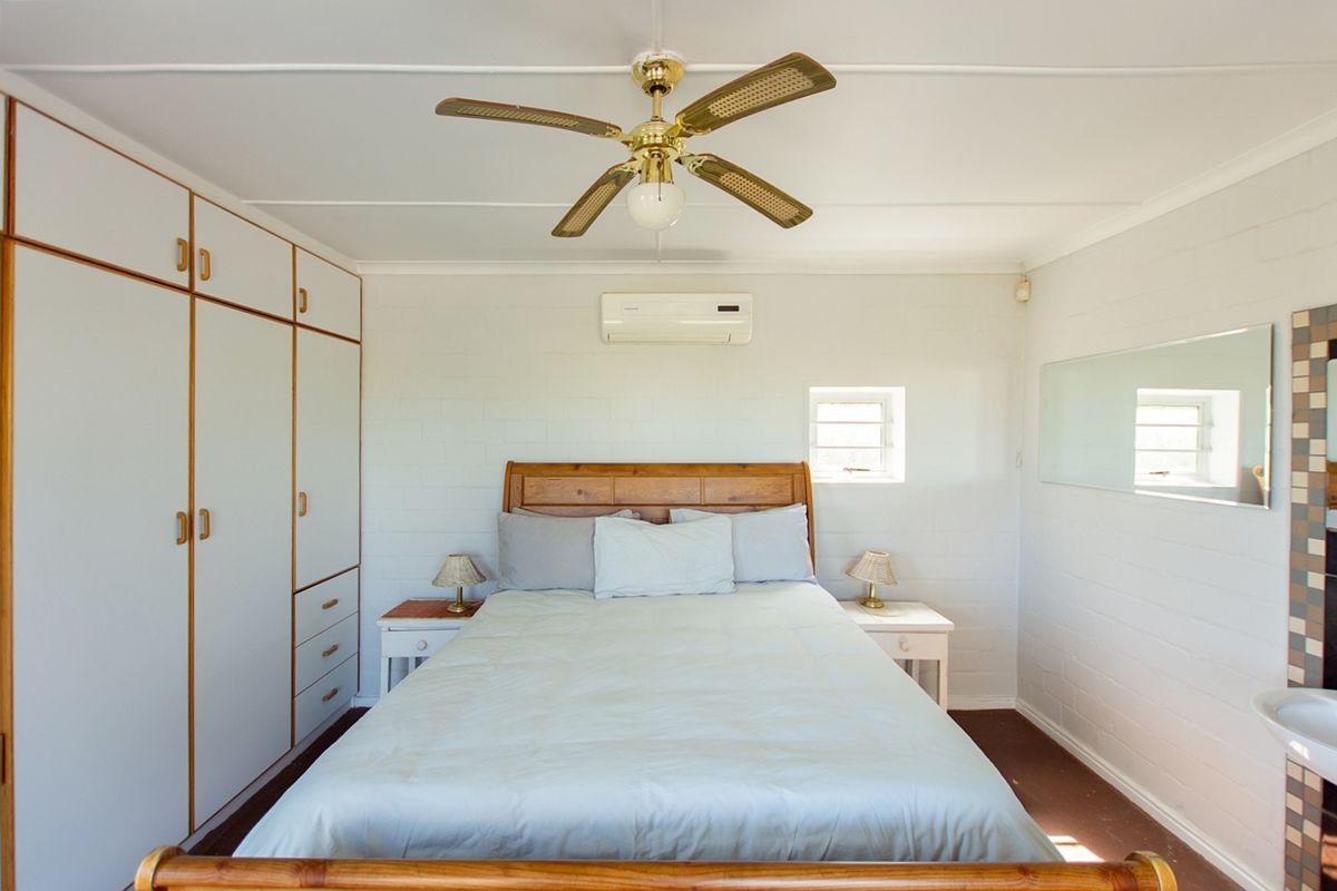 A bedroom featuring built-in cupboards, a ceiling fan, and a wall-mounted air conditioning unit, providing functional storage and climate control.