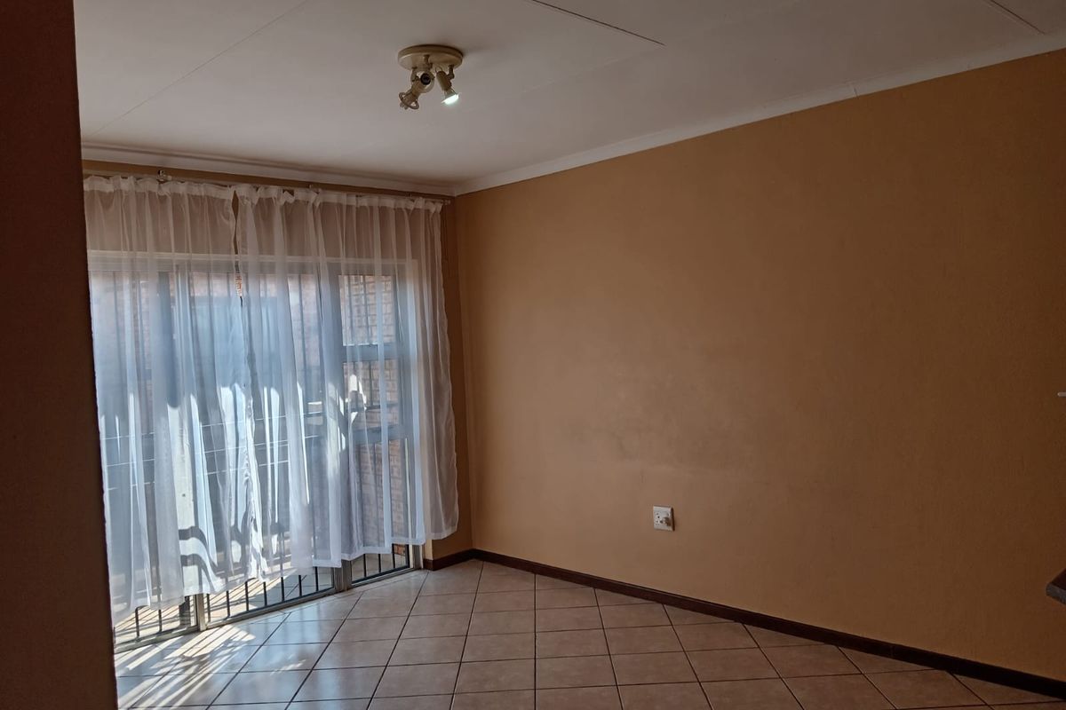 An empty living room featuring tiled flooring, a ceiling-mounted light fixture, and a sliding glass door leading to an outdoor area.