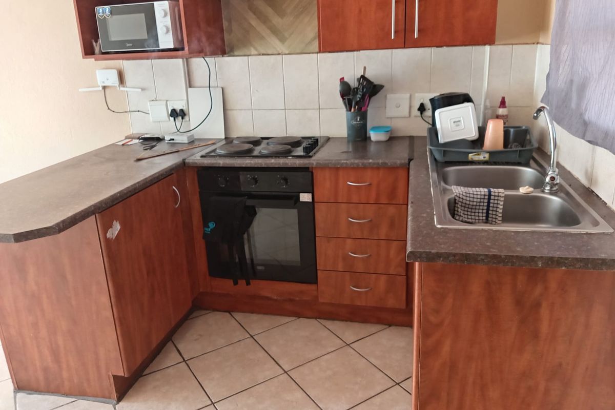 A functional kitchen featuring wood-look cabinetry, a built-in oven with electric hob, tiled backsplash, and a double-basin stainless steel sink.