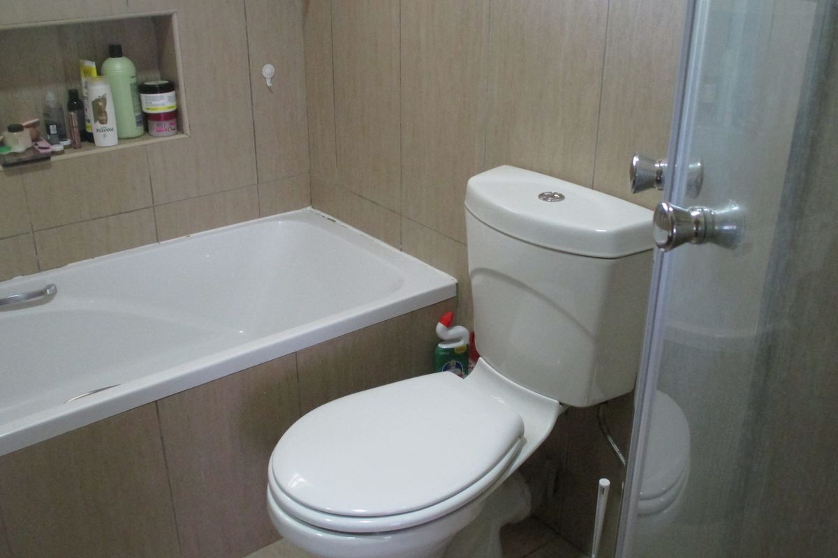 A functional bathroom featuring a built-in bathtub, a separate shower enclosure, and a recessed wall niche for storage, finished with neutral wall tiles.