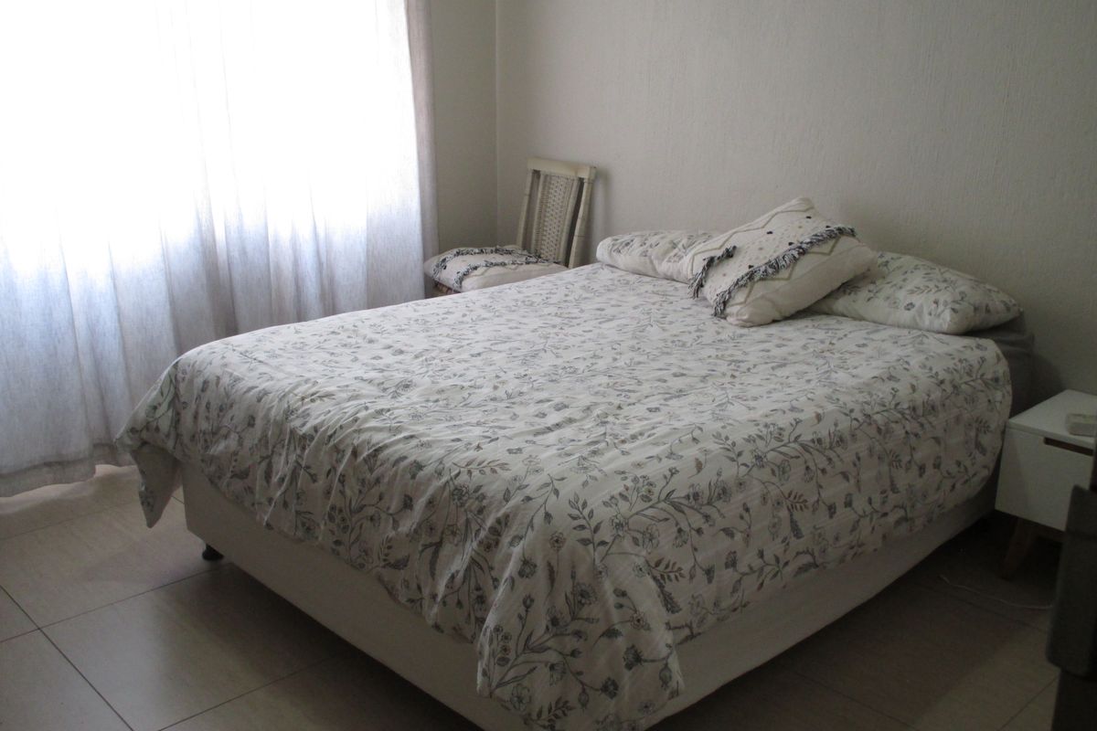 A functional bedroom featuring neutral tiled flooring and natural light through window curtains.
