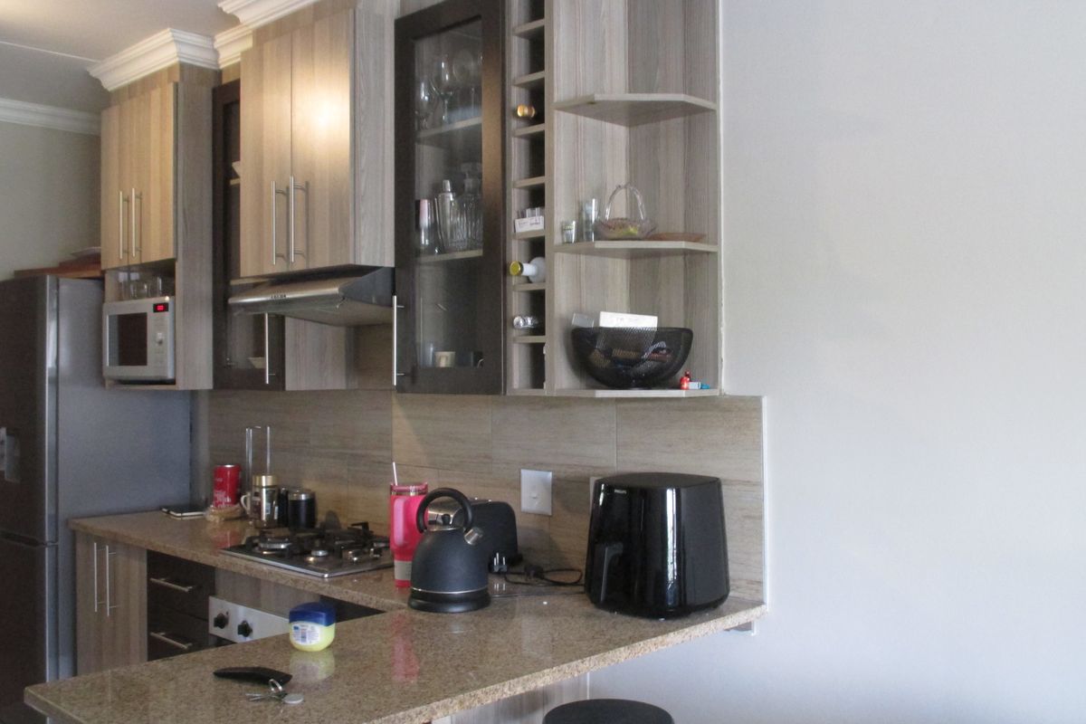 Modern kitchen featuring light wood-grain cabinetry, granite countertops, a gas hob with extractor fan, and a built-in microwave, finished with a tiled backsplash.